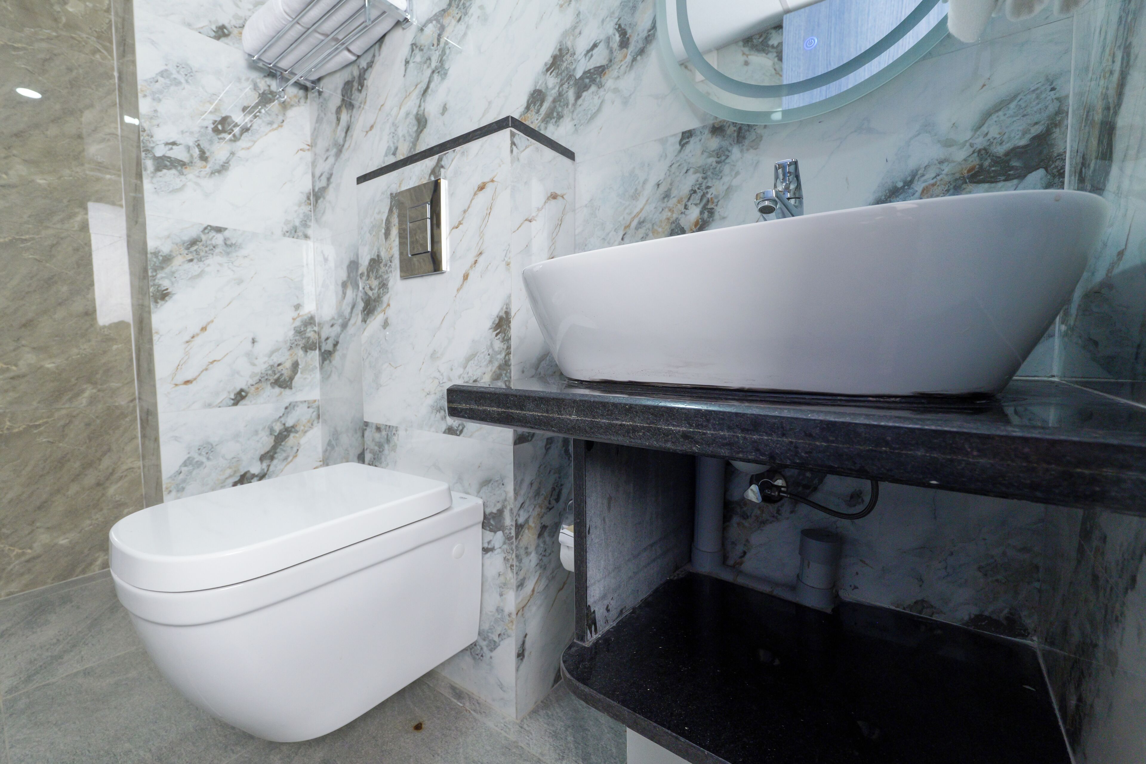 Um banheiro com vaso sanitário branco, pia preta e painel de backsplash de mármore.