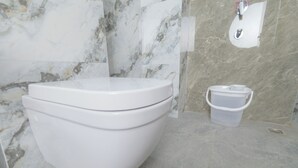 Un baño moderno con inodoro blanco, pared de mármol y un pequeño cubo de basura.