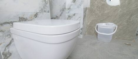 A modern bathroom with a white toilet, a marble wall, and a small trash bin.