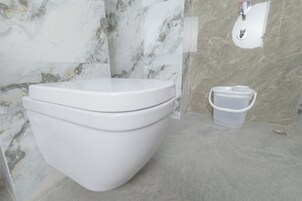 Un baño moderno con inodoro blanco, pared de mármol y un pequeño cubo de basura.