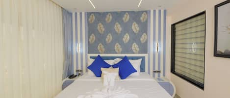 Ein Hotelzimmer mit einem ordentlich bezogenen Bett, einem Kopfteil mit dekorativen Verzierungen, einem Nachttisch mit Lampe und einem Fenster mit Jalousien.