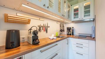 A modern kitchen with white cabinets, a wooden countertop, and various kitchen appliances.