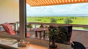 A balcony with a view of a green landscape and the sea. There is a table with two glasses and a cup, a chair, and a potted plant. - Vacation Rental in Husum with an Exceptional Ocean View and a Balcony (Husum)