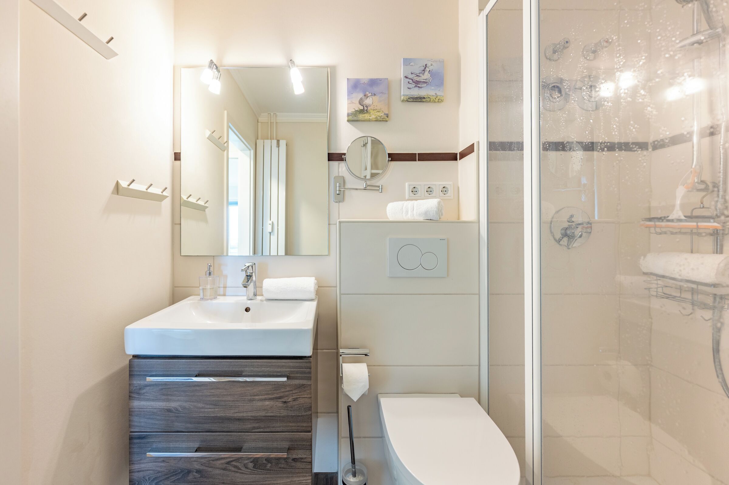 Ein modernes Badezimmer mit Waschbecken, Spiegel und Toilette. Eine Dusche mit Glastür und ein Handtuchhalter sind ebenfalls vorhanden.