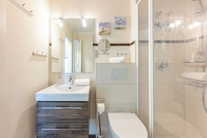 A modern bathroom with a white sink, mirror, and toilet. There is a shower with a glass door and a towel rack. - Vacation Rental in Husum with an Exceptional Ocean View and a Balcony (Husum)