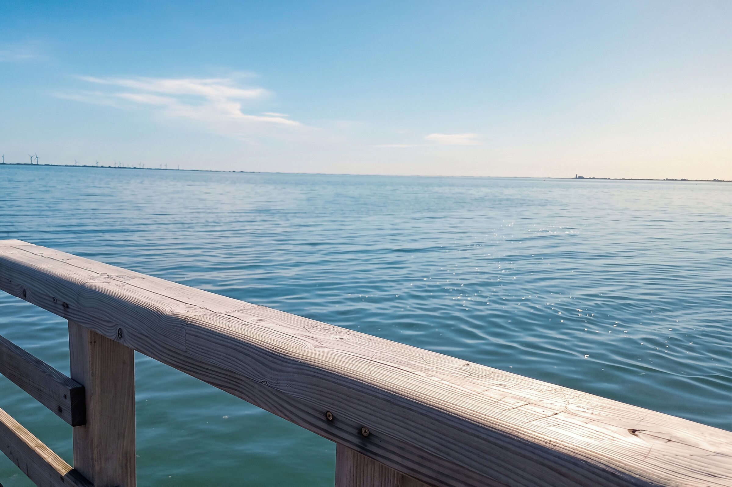 Eine Holzstege, der sich in ruhiges Wasser erstreckt, mit blauem Himmel darüber.