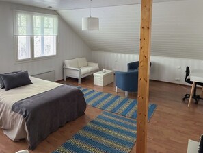 Un dormitorio con cama, sofá blanco, silla azul, escritorio y estructura de vigas de madera.