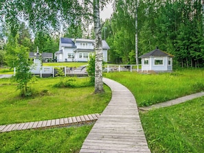 A wooden pathway leading to a house with a large deck and a smaller structure nearby.