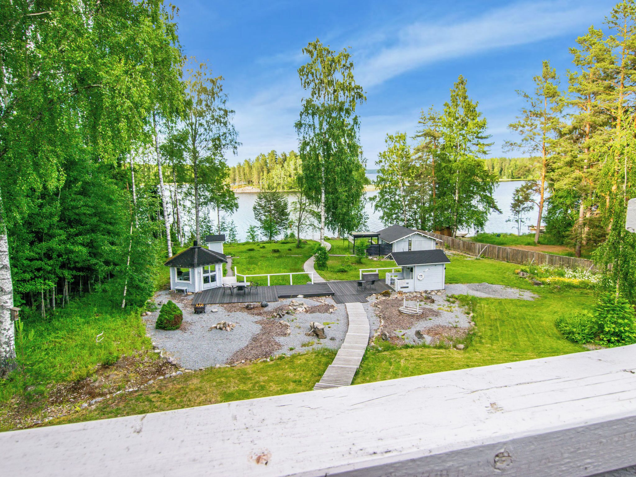 En ejendom ved søen med to hytter, en terrasse og et bålsted.