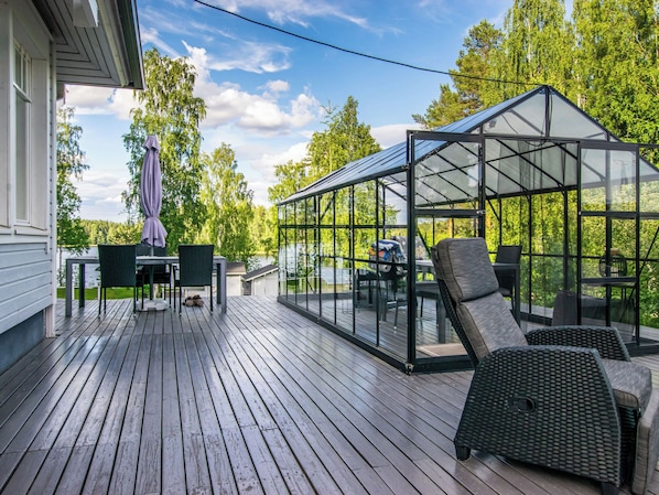 A covered outdoor deck with a glass enclosure, wicker furniture, and a view of a lake.