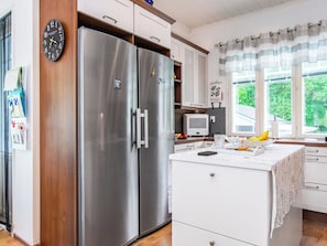 A kitchen with stainless steel appliances, a microwave, and a window with curtains.