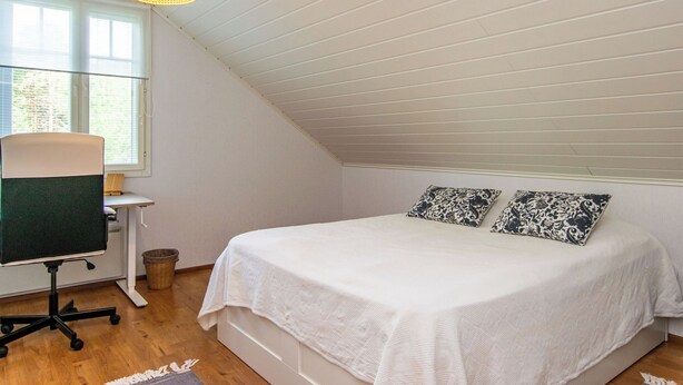 A bedroom with a bed, two patterned pillows, a desk with a chair, a computer, and a hanging light fixture.