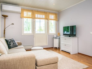 A living room with a sofa, ottoman, TV, and a small side table.