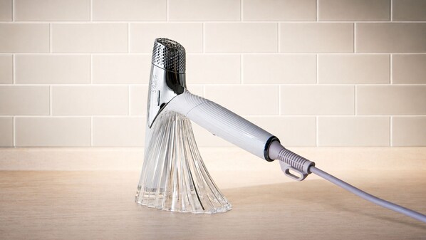 A clear object with a handle and a textured top, placed on a flat surface against a tiled wall.