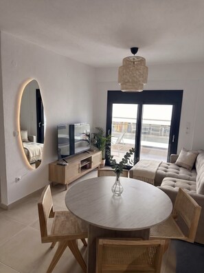 Een moderne woonkamer met een ronde eettafel, banken, een televisie en een groot raam.