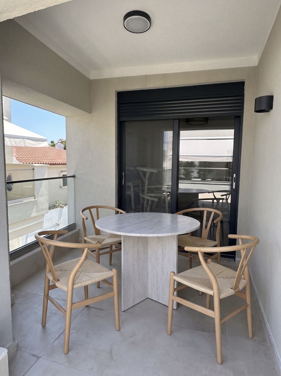 A balcony with a round table and four chairs, a sliding glass door, and a view of buildings.