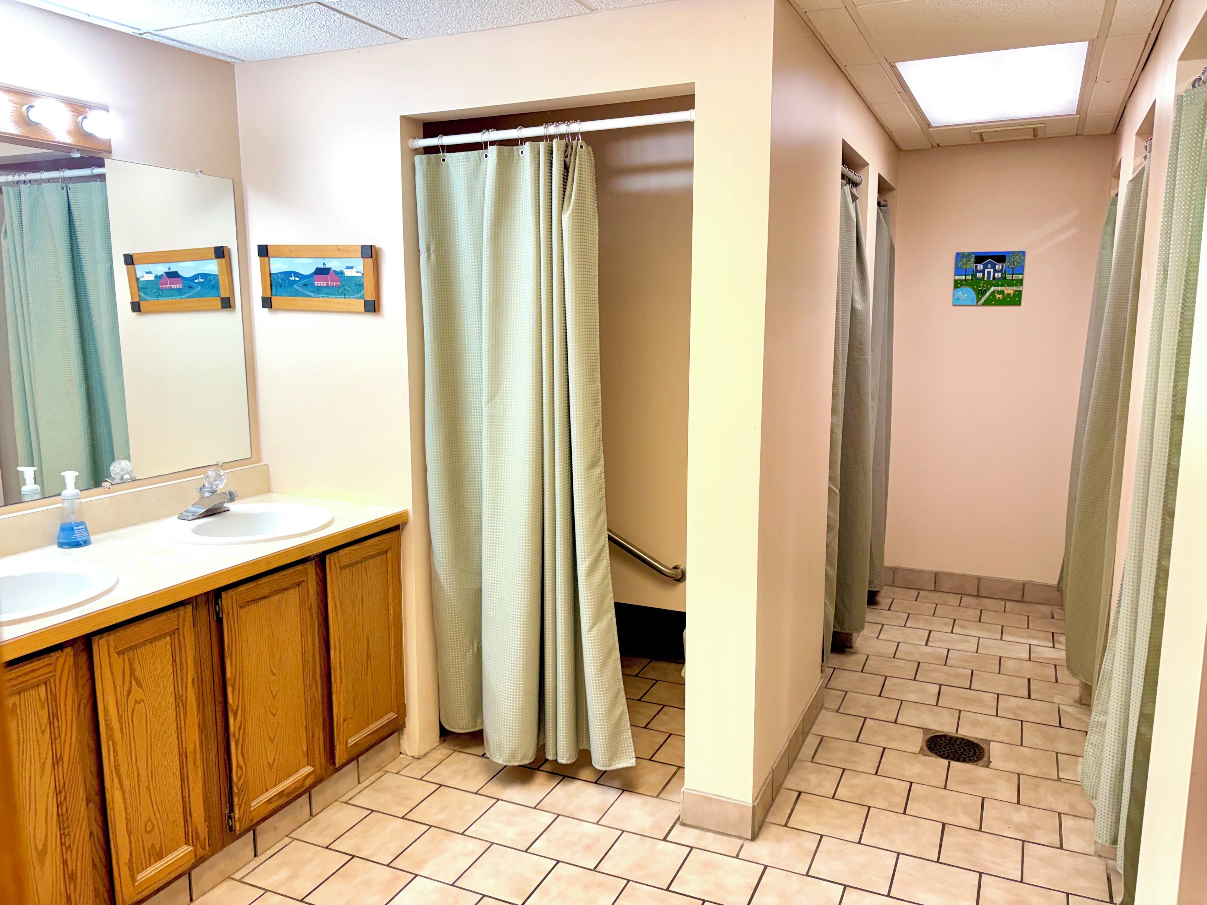 Une salle de bain avec deux lavabos, des meubles en bois, un rideau de douche et un carrelage au sol.