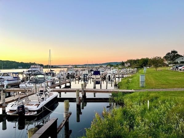 A marina with boats docked at wooden piers, surrounded by grassy areas and a clear sky.