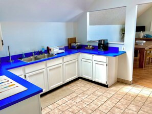 Een keuken met witte kastjes, een blauw aanrecht, een koffiezetapparaat en een spoelbak.