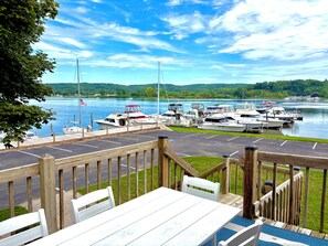 A marina with boats docked, a wooden deck, and a view of a lake with hills in the background.
