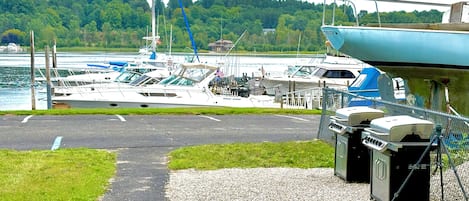 Un puerto deportivo con barcos amarrados, una zona verde y un camino de grava que lleva a una zona cubierta con parrillas para barbacoa.