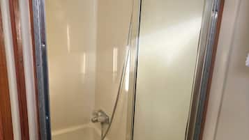 Pequeño espacio de ducha cerrado con puerta de cristal, cabezal de ducha y un tapete azul en el suelo.