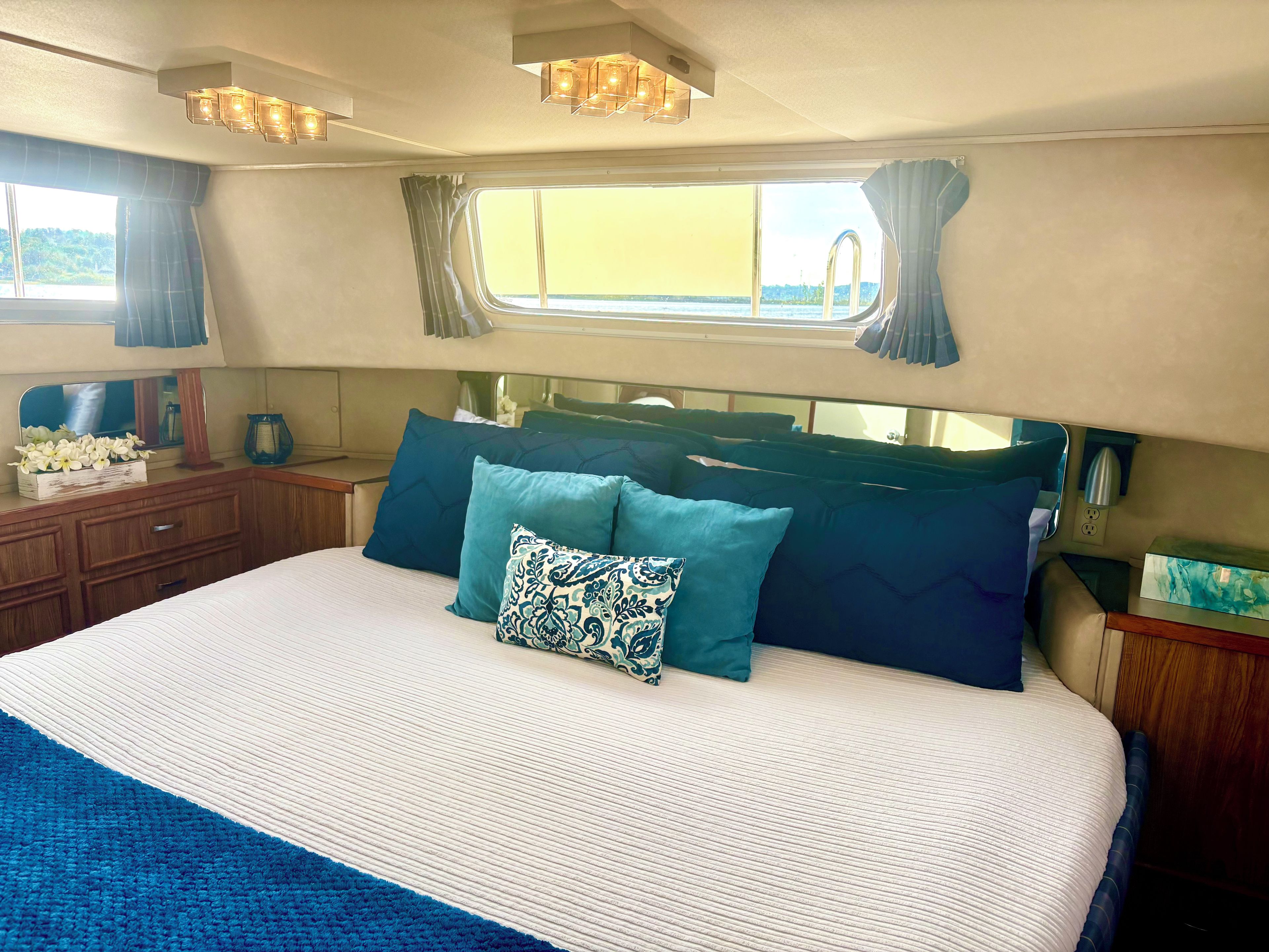 Ein Schlafzimmer mit einem Bett, Kissen, einem Nachttisch, einer Kommode und einem Fenster mit Vorhängen.