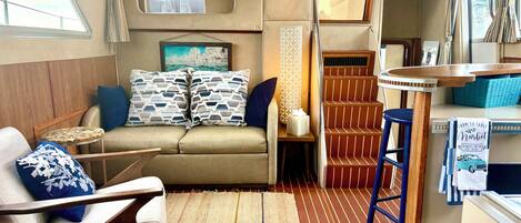 A compact interior with a sofa, a small table, a bar stool, and a staircase.