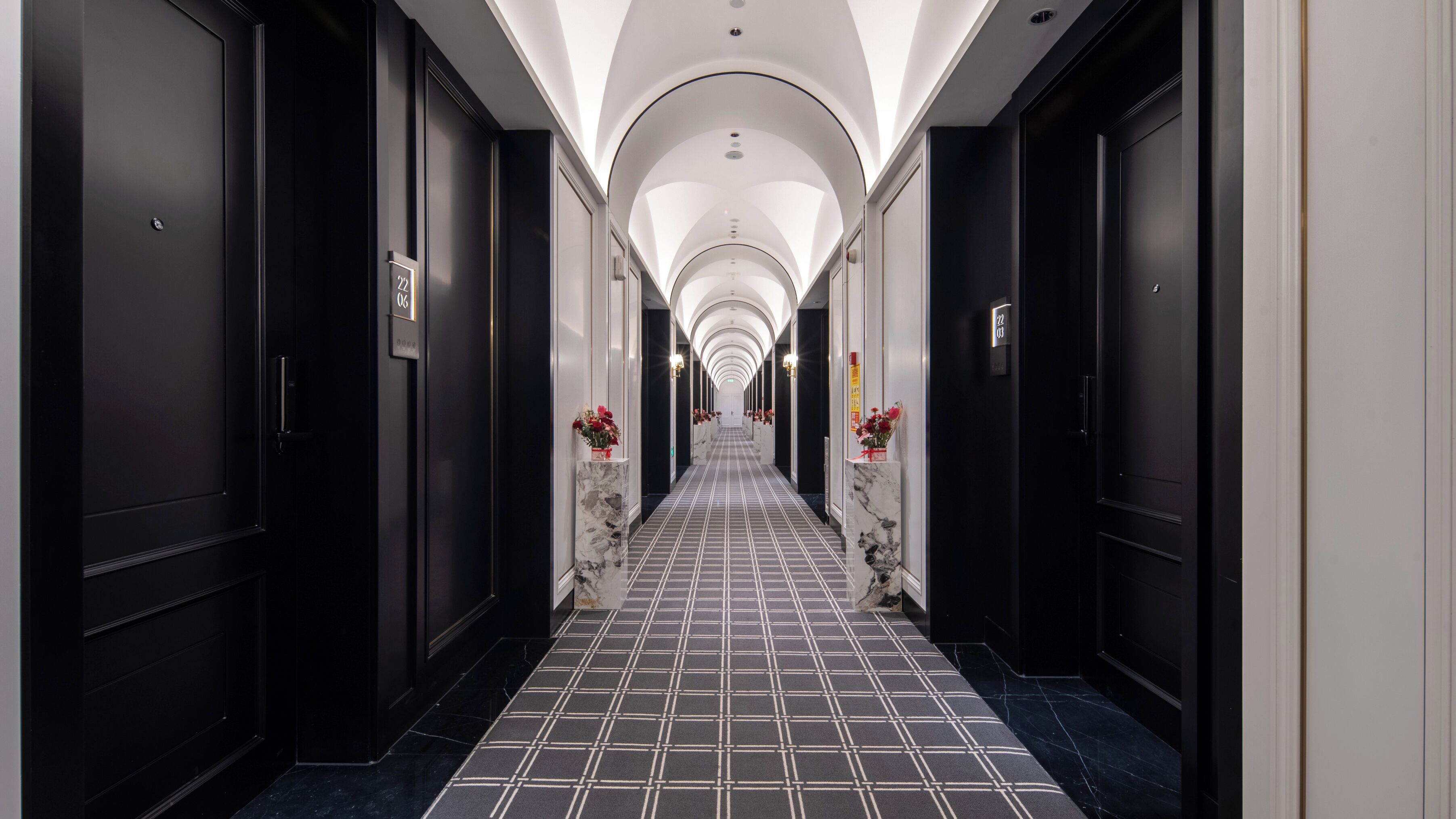 A hotel corridor with black doors, numbered room signs, and a tiled floor.