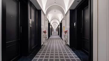 A hotel corridor with black doors, numbered room signs, and a tiled floor.