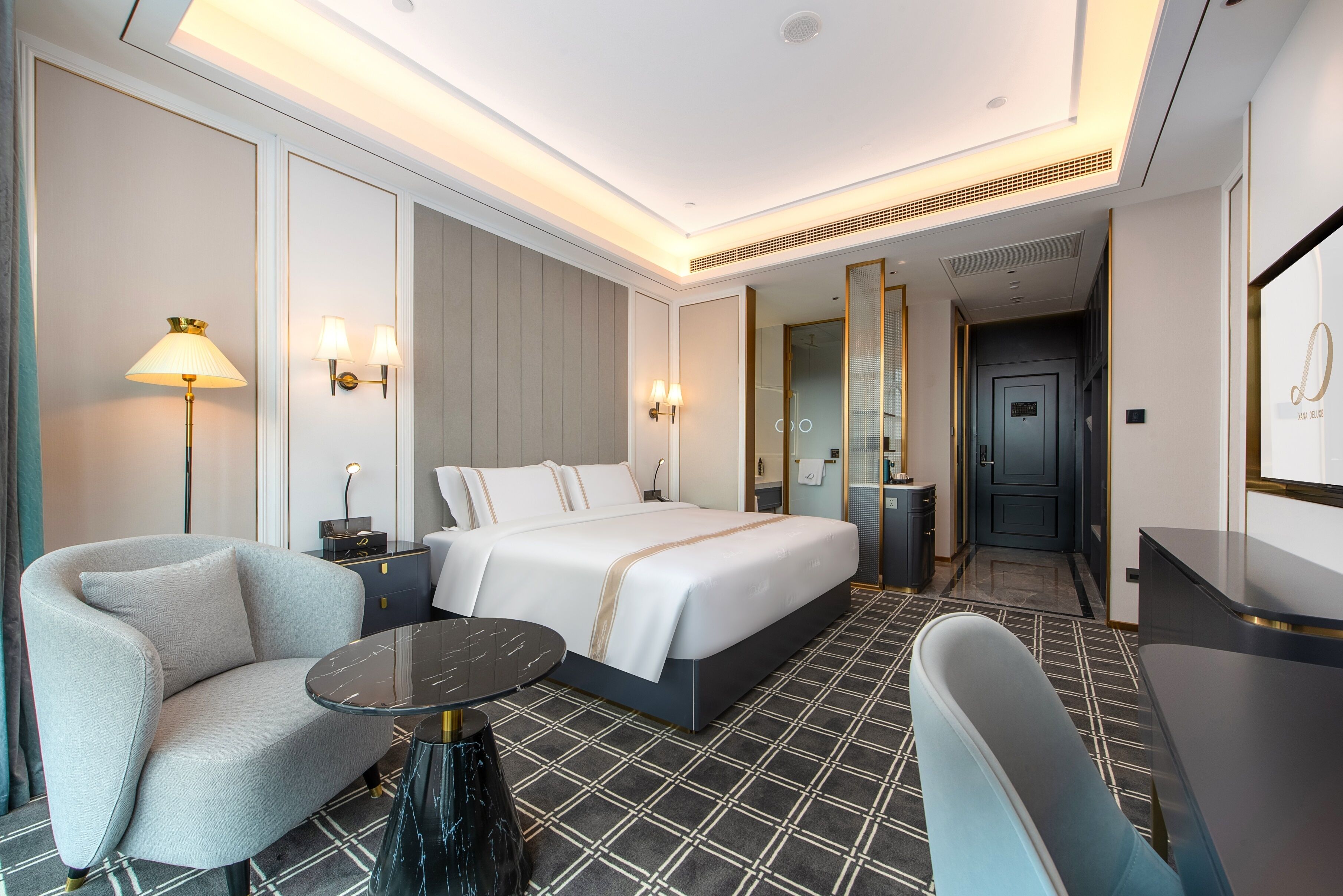Quarto de hotel com cama, duas cadeiras, uma mesinha e escrivaninha.