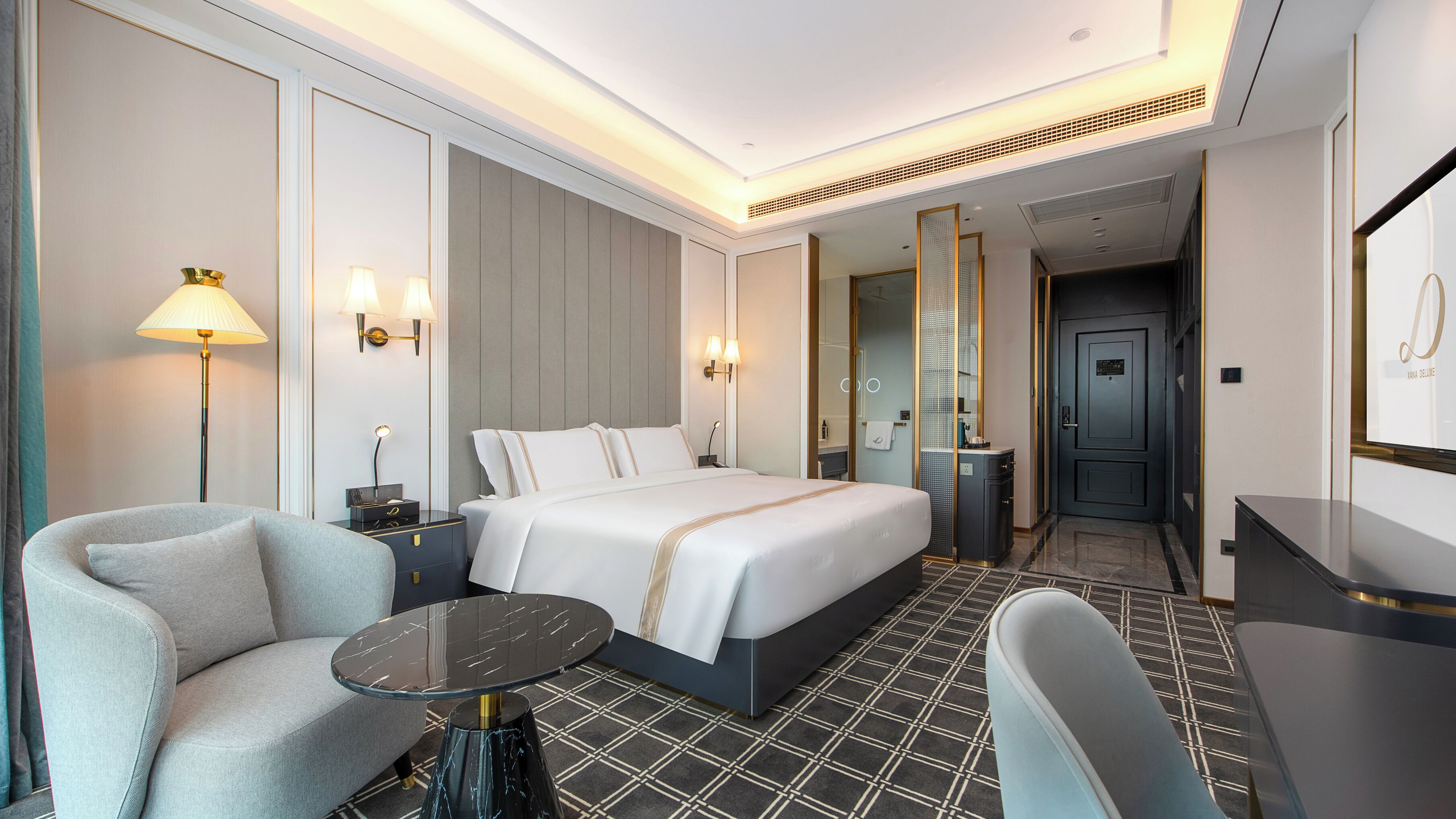 A hotel room with a bed, a seating area with a table, a desk, and a mirror.