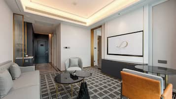 Habitación de hotel con sofá, sillón, una mesita redonda y una pantalla de televisión que muestra un logotipo.