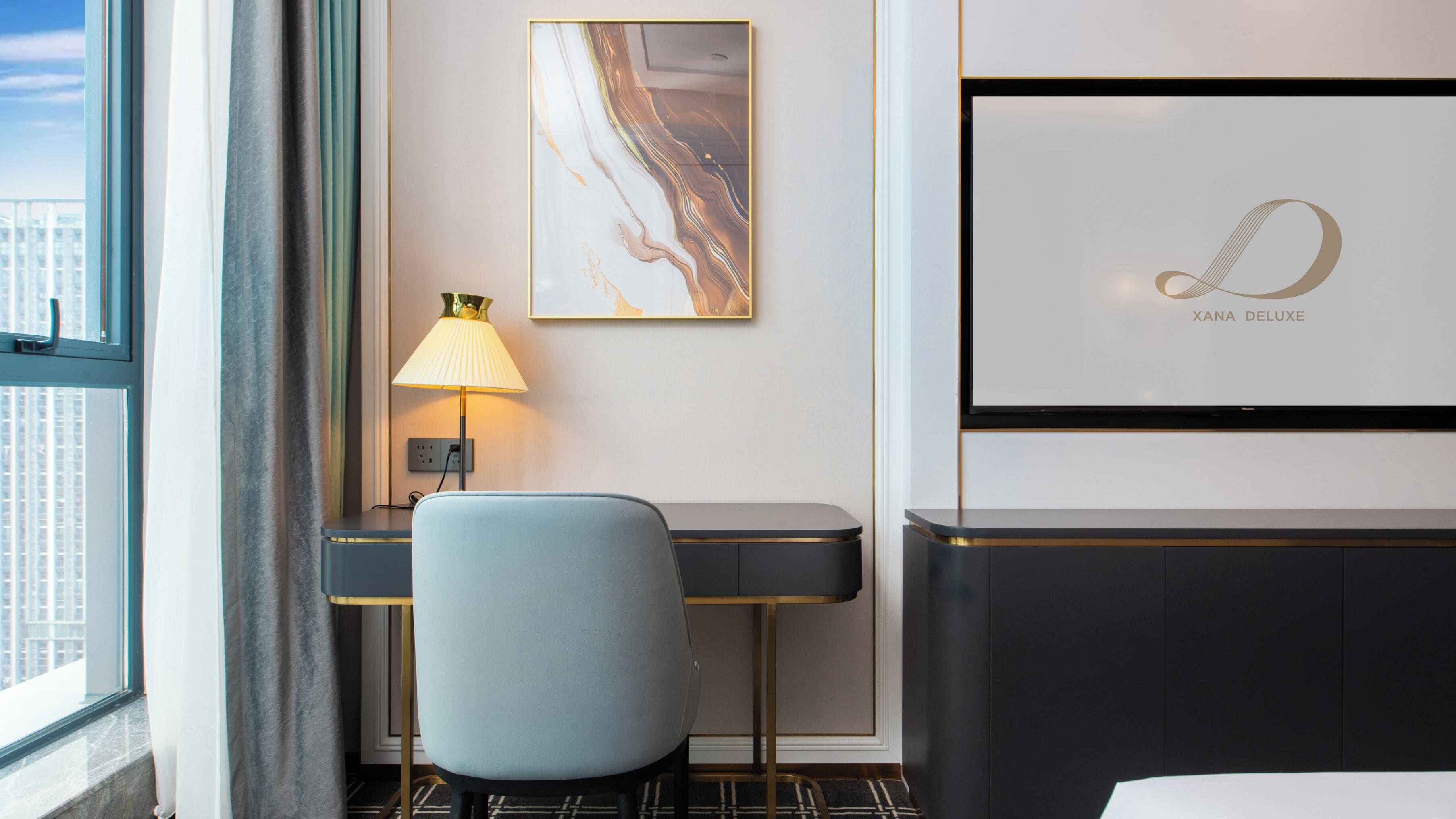 Habitación de hotel con escritorio, silla, lámpara, una obra de arte y una cama.