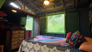 Une chambre à coucher comprenant un lit, un ventilateur de plafond, une commode et une fenêtre donnant sur un paysage verdoyant.