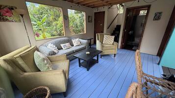 Une pièce avec un plancher en bois bleu, un canapé, deux fauteuils, une table basse et une chaise en osier.