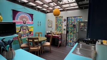A kitchen with a blue countertop, wooden chairs, a dining table, and a colorful tapestry on the wall.