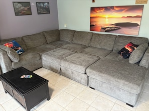 A grey sectional sofa with two decorative pillows, a black coffee table with a floral design, and a wall with three framed pictures.