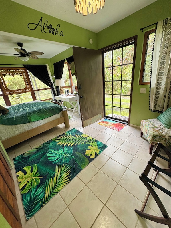 A room with a bed, a rocking chair, a desk, and a door leading to an outdoor area.