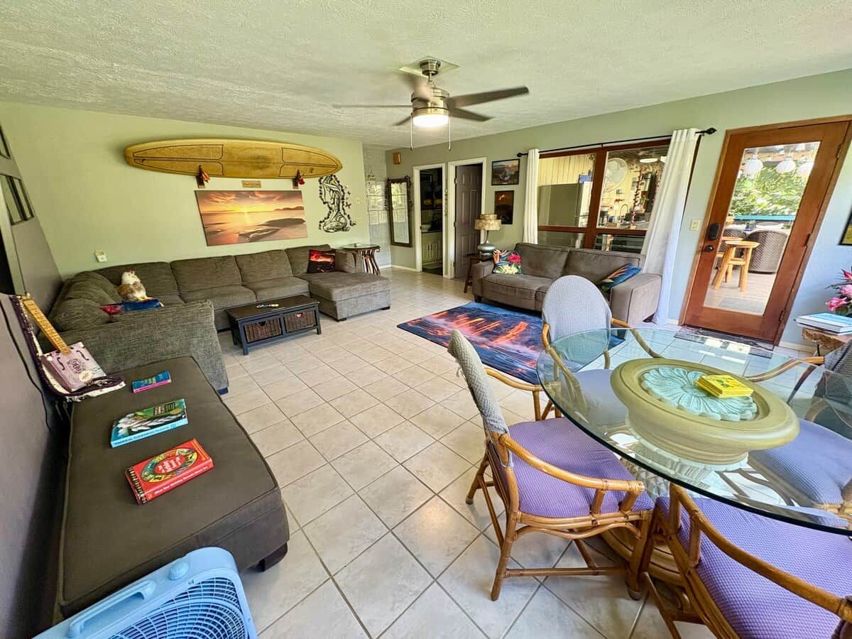 Un salon avec un canapé, une table à manger avec un plateau en verre et un ventilateur de plafond.
