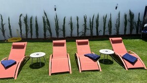 Four lounge chairs with small tables, arranged on a grassy lawn with a row of tall plants against a wall. - Elegant villa in the Assilah countryside. Peace and luxury (Asilah)