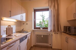 A compact kitchen with a window, a radiator, a microwave, and a wooden cutting board. - Vacation Rental No. 5, 50 square meters, 1 bedroom, bay window, terrace (Oberaudorf)