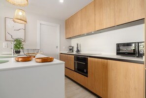 A modern kitchen with wooden cabinets, a built-in oven, and a microwave. - Los Colibríes by H - Isla Canela Golf GLHC7002P104 (Ayamonte)