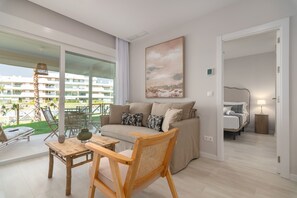 Een moderne woonkamer met een bank, een houten stoel, een bijzettafeltje en een schilderij aan de muur.