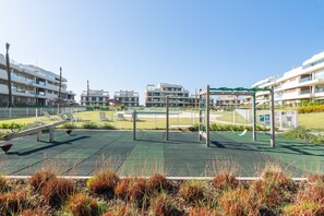 Ein Spielplatz mit unterschiedlicher Spielausstattung, umgeben von einem Zaun, mit Wohnhäusern im Hintergrund.