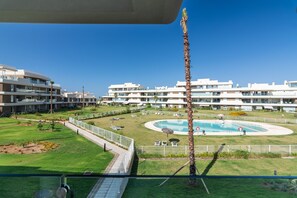 A modern apartment complex with a central swimming pool, surrounded by well-maintained lawns and palm trees. - Los Colibríes by H - Isla Canela Golf GLHC7012P102 (Ayamonte)