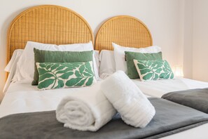 A bed with a woven headboard, white linens, and green leaf-patterned pillows. - Los Colibríes by H - Isla Canela Golf GLHC7012P102 (Ayamonte)