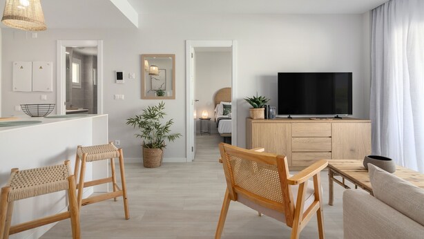 Ein modernes Wohnzimmer mit Fernseher, Holzmöbeln und einer Küchenzeile mit weißer Arbeitsplatte.