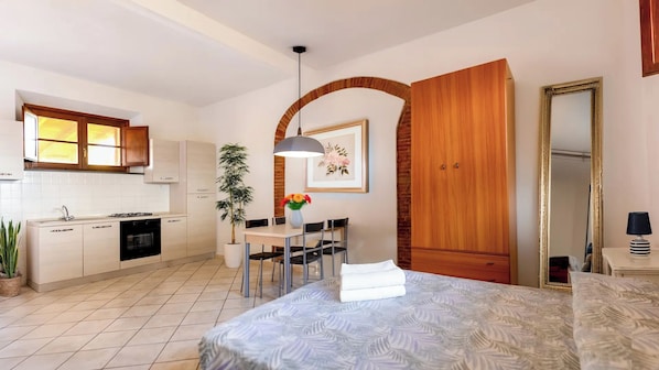 A modern hotel room with a bed, a dining area, a kitchen, and a large wooden wardrobe.