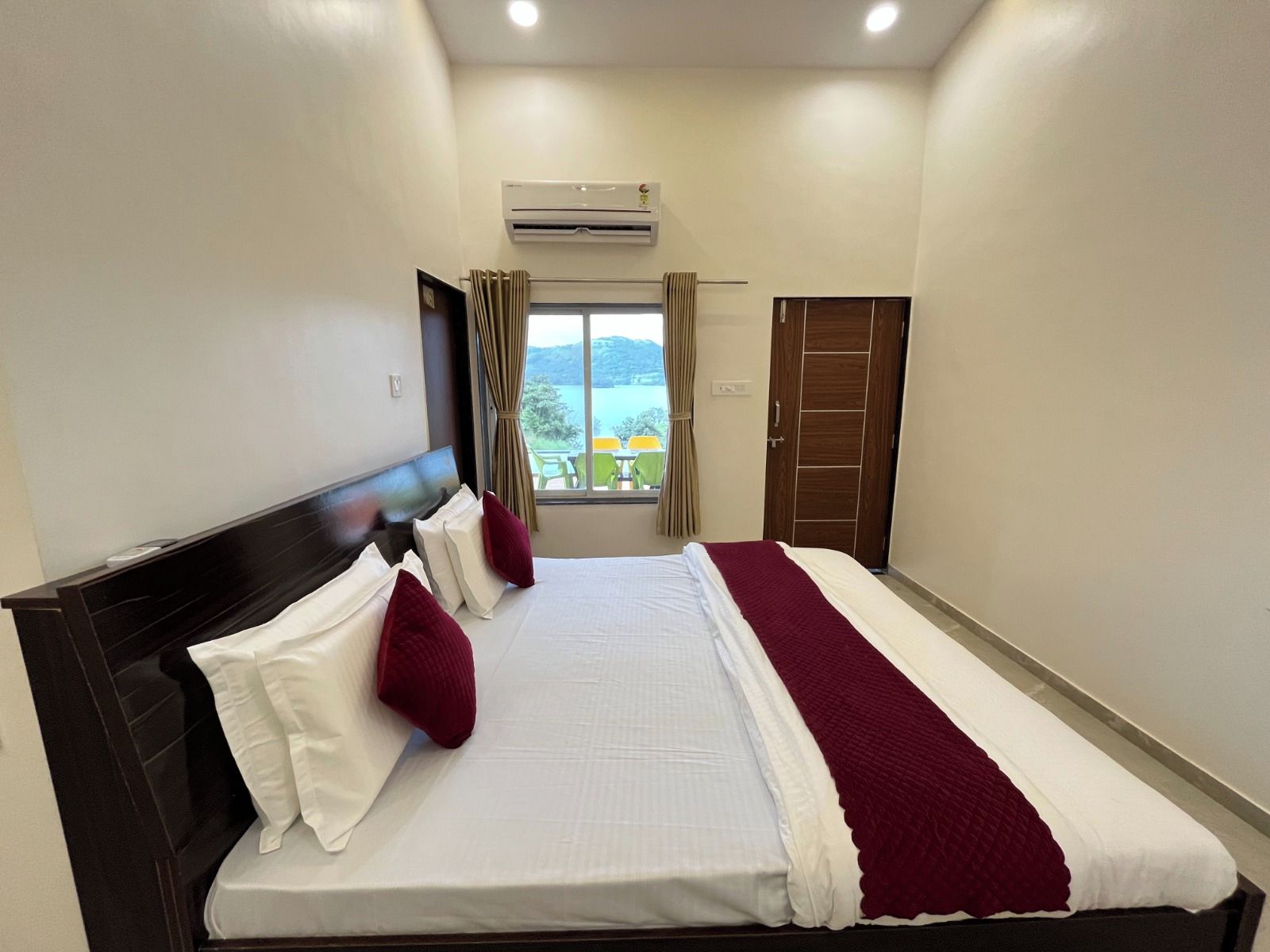 A hotel room with a bed, a window with curtains, an air conditioning unit, and a door.